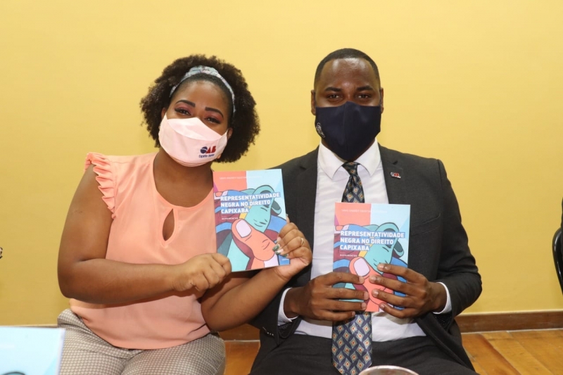 O ex-presidente, Savio Faustino, e a atual presidente, Hellen Tiburcio Tiago Marinho, da Comissão de Igualdade Racial, mostram o livro